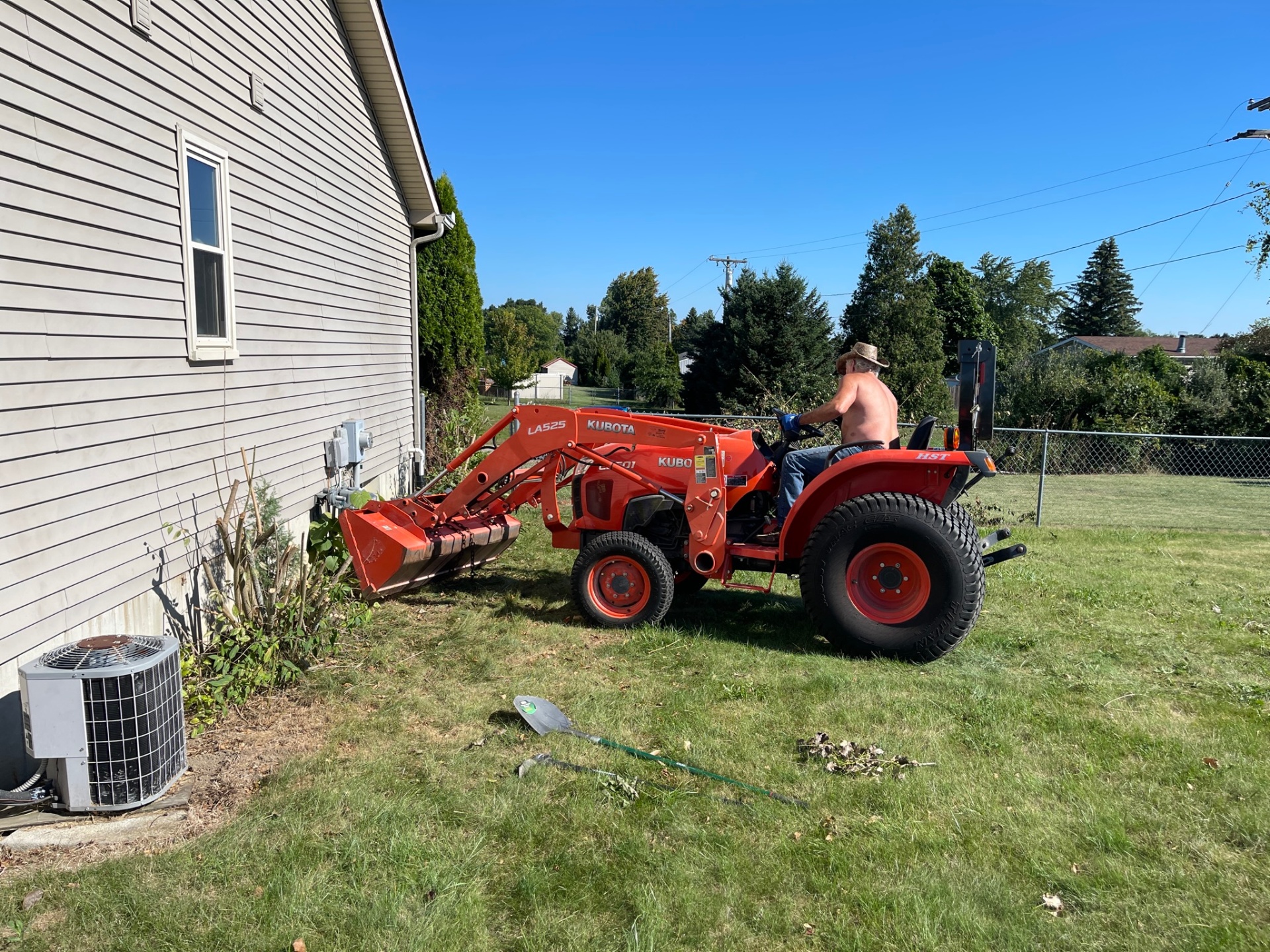 Kubota tractor clearing overgrowth along the side of a home in Lapeer, MI