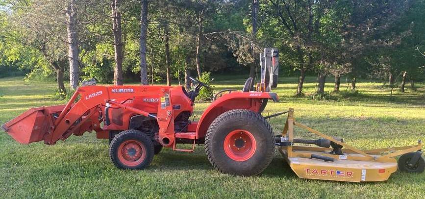 Kubota tractor with brush hog mower clearing an overgrown field